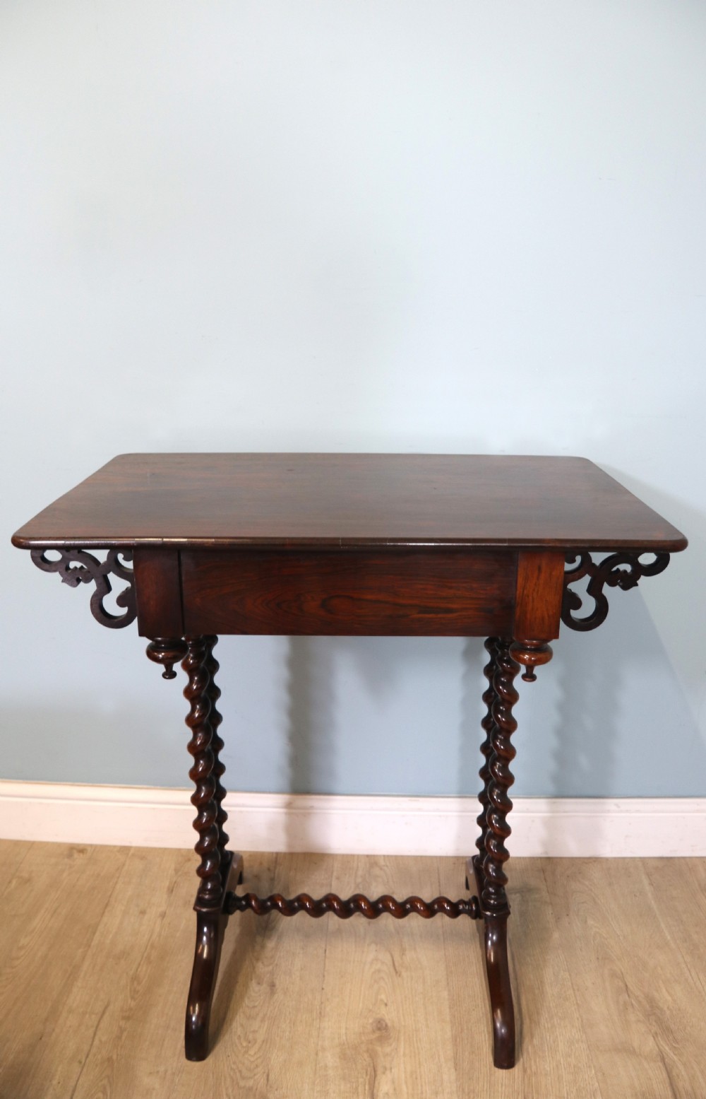 A 19th-century dark rosewood sewing table featuring barley twist legs, side fretwork brackets, a single drawer, and a blue fabric work basket below. View XXIV