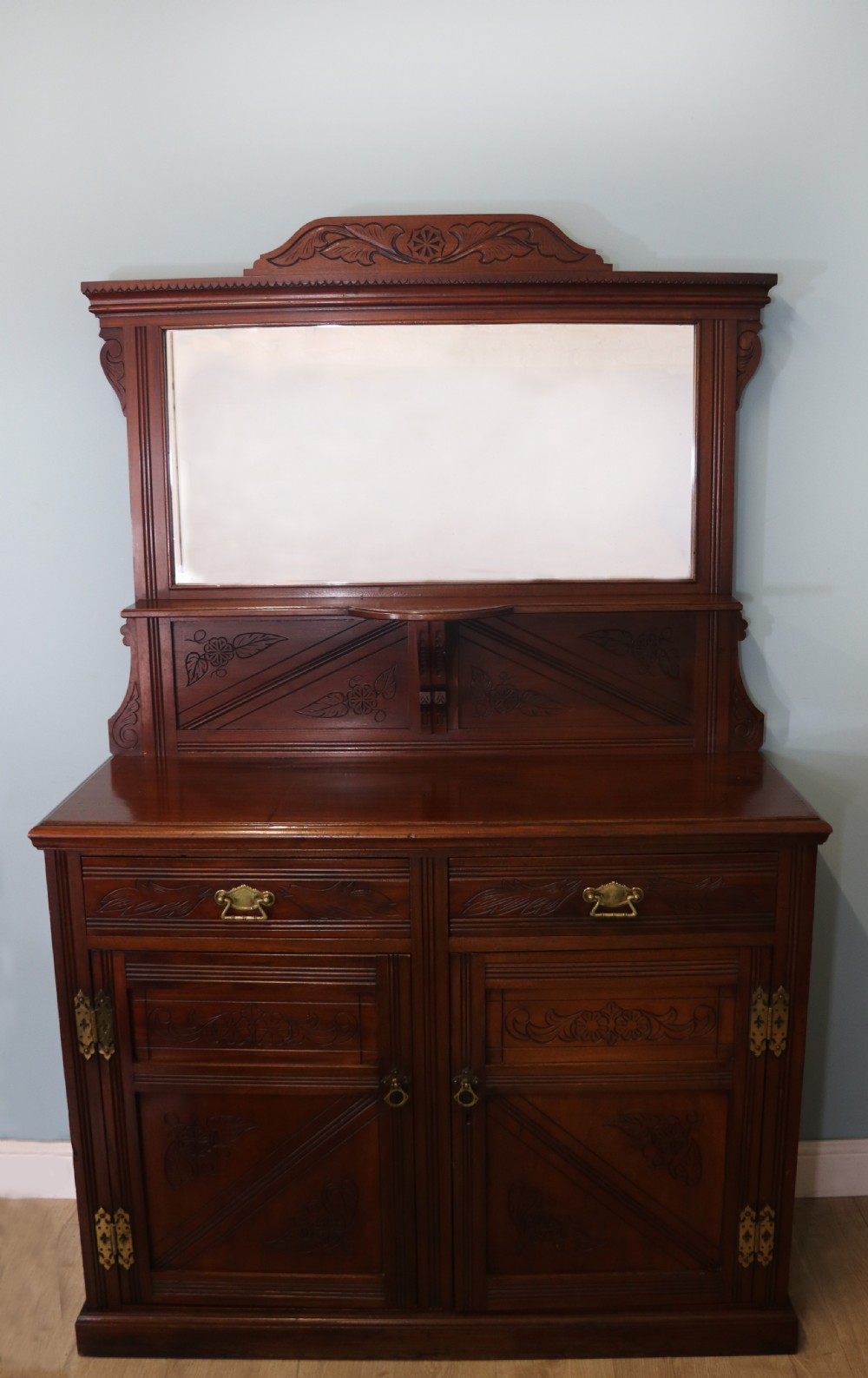 A Victorian American walnut sideboard featuring a mirrored gallery back, carved floral panels, two upper drawers, and two lower cupboard doors.
