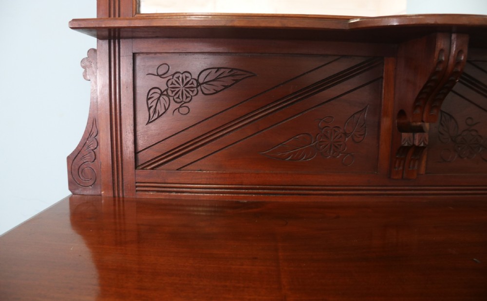 A Victorian American walnut sideboard featuring a mirrored gallery back, carved floral panels, two upper drawers, and two lower cupboard doors. View X