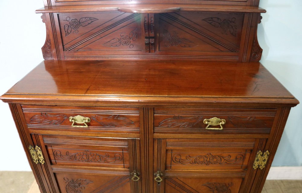 A Victorian American walnut sideboard featuring a mirrored gallery back, carved floral panels, two upper drawers, and two lower cupboard doors. View XIII