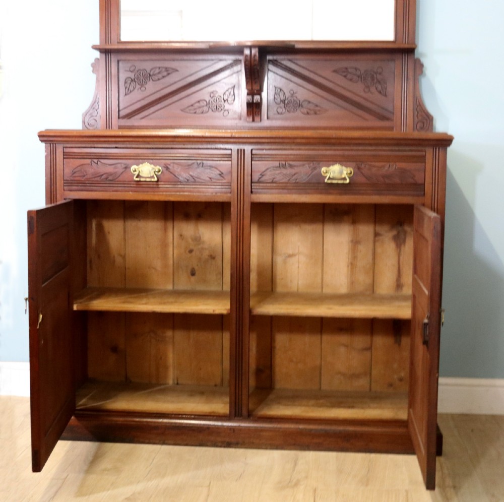 A Victorian American walnut sideboard featuring a mirrored gallery back, carved floral panels, two upper drawers, and two lower cupboard doors. View XIV