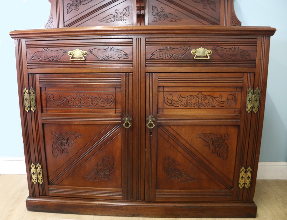 A Victorian American walnut sideboard featuring a mirrored gallery back, carved floral panels, two upper drawers, and two lower cupboard doors. View XV