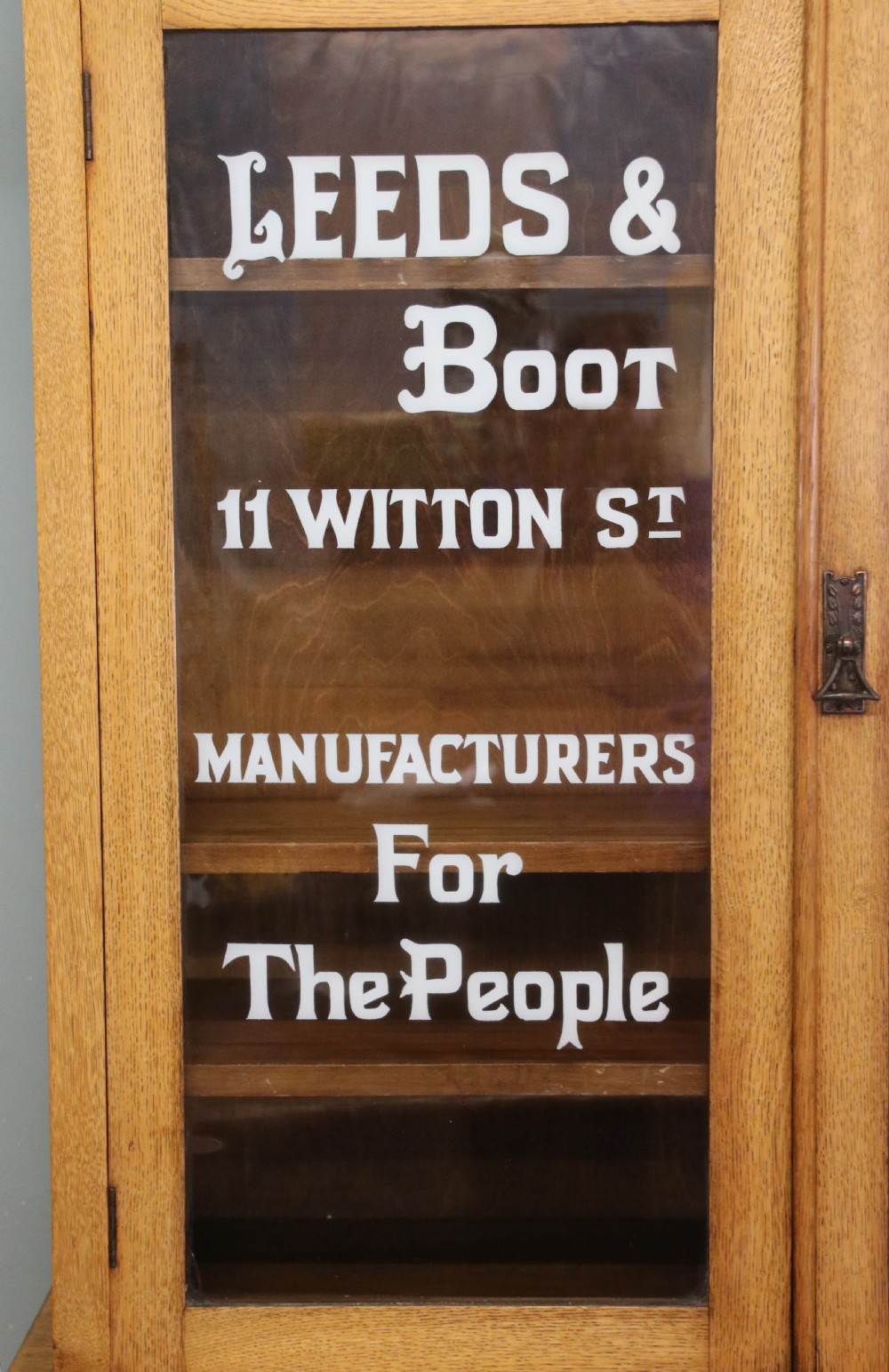 A late nineteenth-century light oak display cabinet featuring glazed upper doors and panelled lower doors decorated with hand-painted white commercial signage. View IX