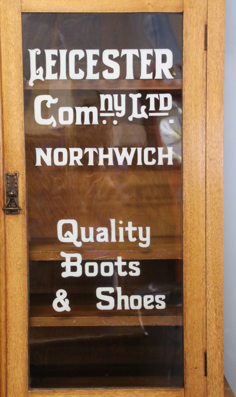A late nineteenth-century light oak display cabinet featuring glazed upper doors and panelled lower doors decorated with hand-painted white commercial signage. View X