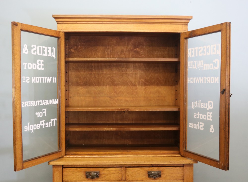 A late nineteenth-century light oak display cabinet featuring glazed upper doors and panelled lower doors decorated with hand-painted white commercial signage. View XI