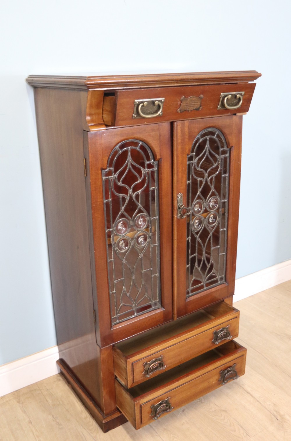 An early 20th-century walnut side cabinet featuring arched leaded glass doors, a top drawer, and two lower drawers with metal handles. View III