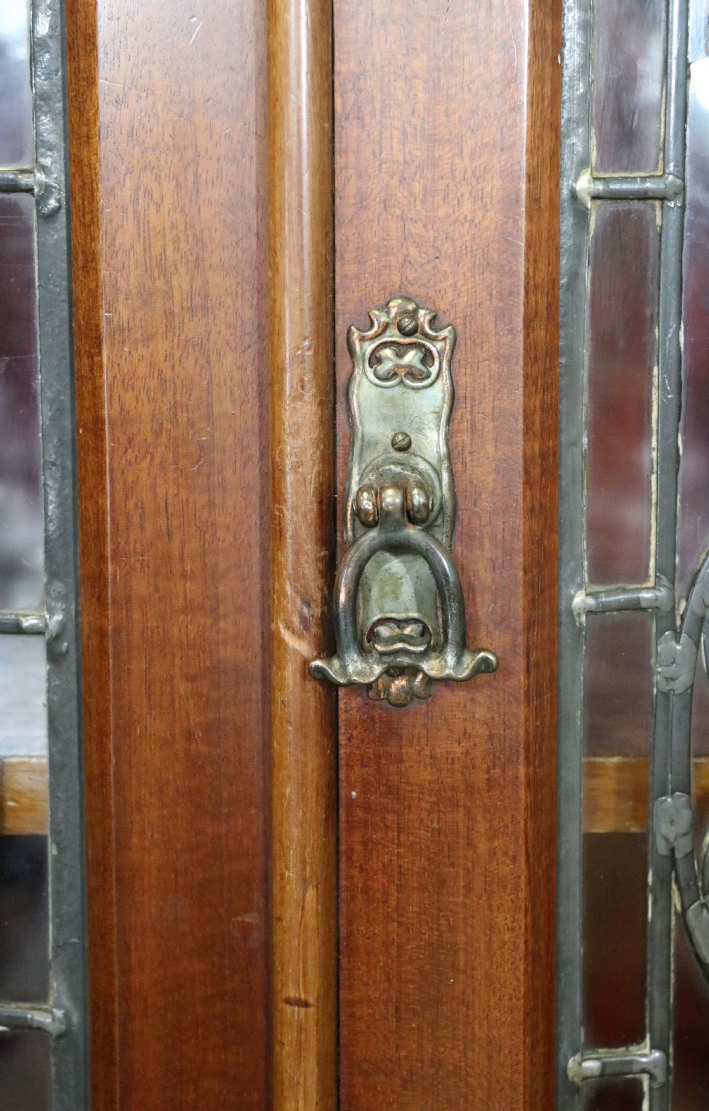An early 20th-century walnut side cabinet featuring arched leaded glass doors, a top drawer, and two lower drawers with metal handles. View IX