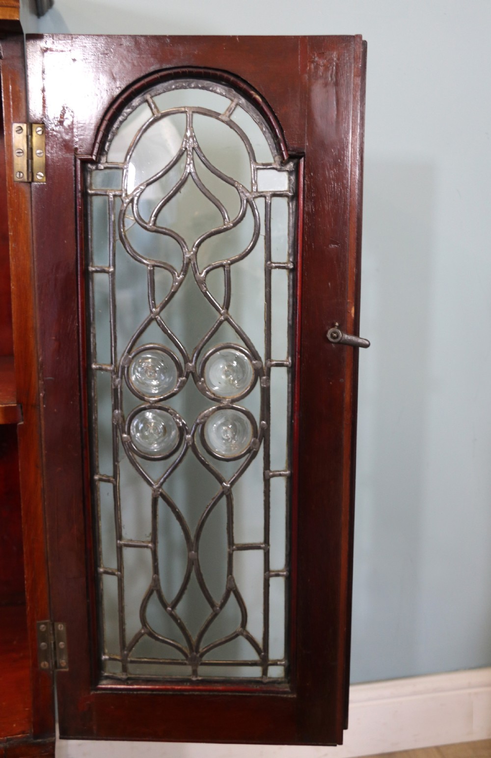 An early 20th-century walnut side cabinet featuring arched leaded glass doors, a top drawer, and two lower drawers with metal handles. View XI