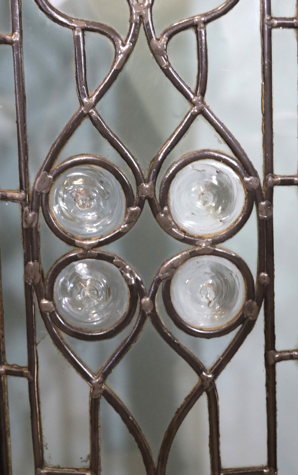 An early 20th-century walnut side cabinet featuring arched leaded glass doors, a top drawer, and two lower drawers with metal handles. View XII