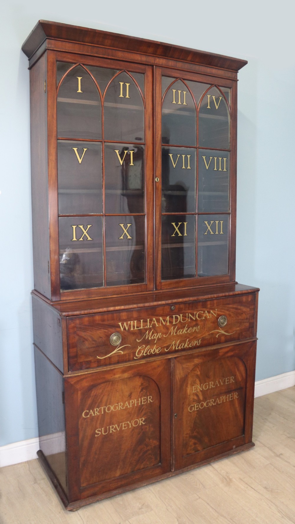 A late Georgian mahogany secretaire bookcase with glazed upper doors featuring Roman numerals, a drop-front fitted writing desk, and two cabinet doors below. View II