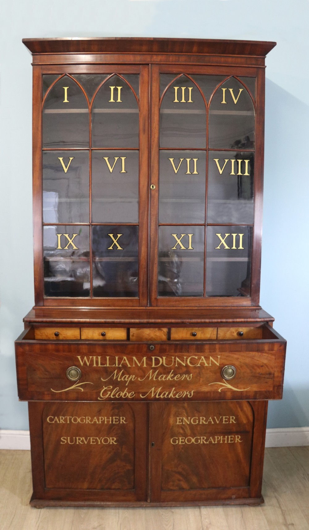 A late Georgian mahogany secretaire bookcase with glazed upper doors featuring Roman numerals, a drop-front fitted writing desk, and two cabinet doors below. View III