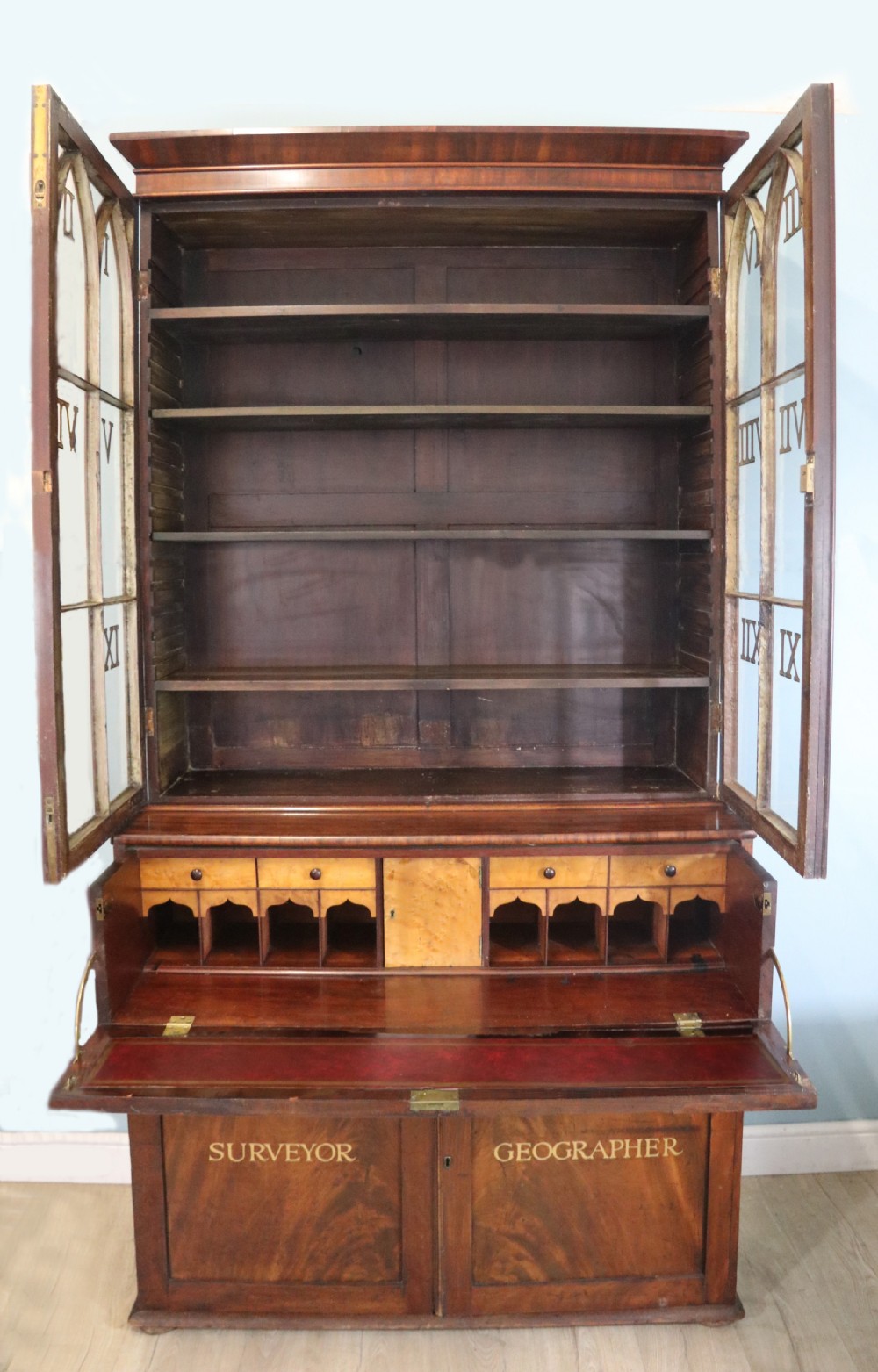A late Georgian mahogany secretaire bookcase with glazed upper doors featuring Roman numerals, a drop-front fitted writing desk, and two cabinet doors below. View IV