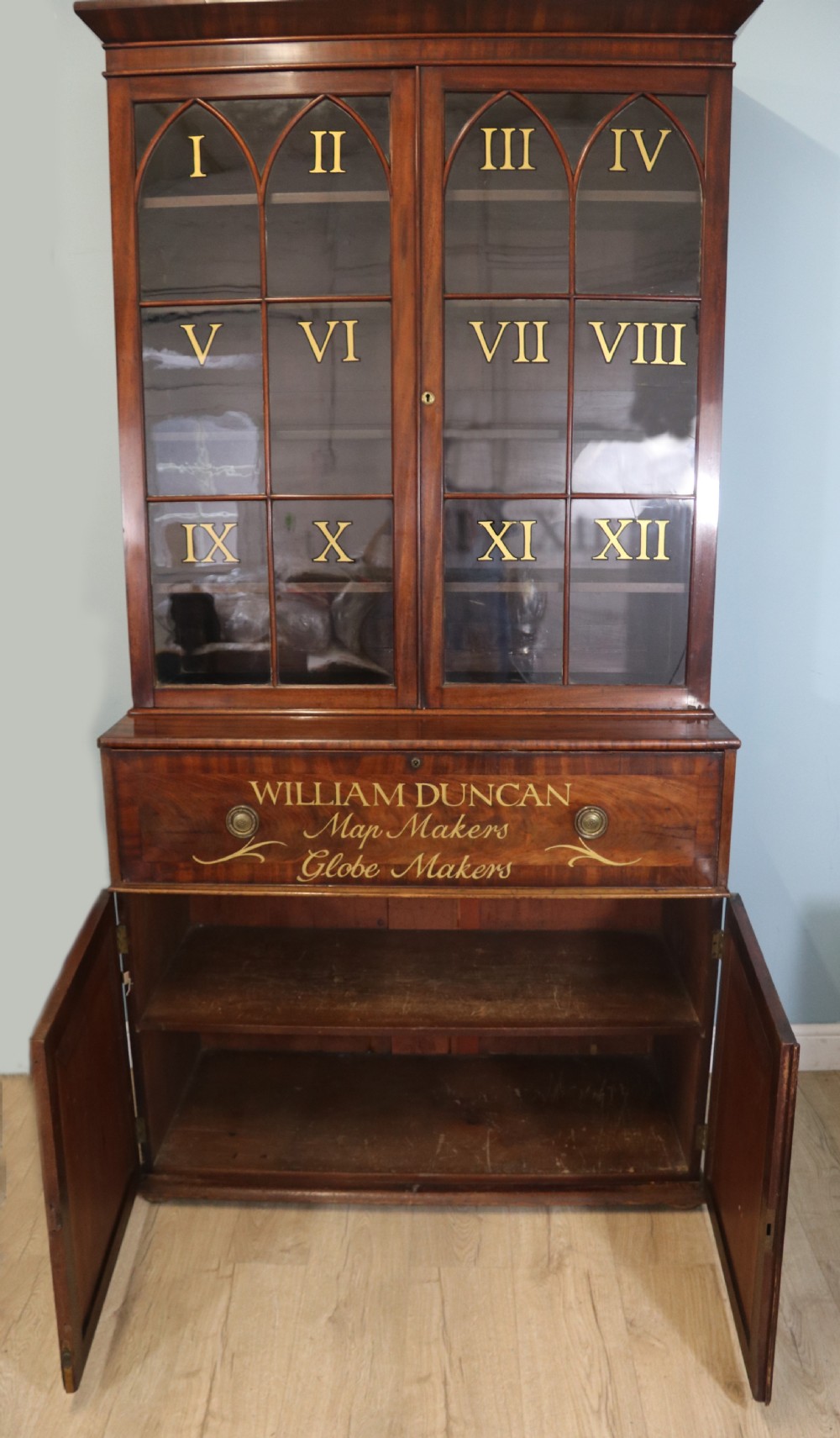 A late Georgian mahogany secretaire bookcase with glazed upper doors featuring Roman numerals, a drop-front fitted writing desk, and two cabinet doors below. View V