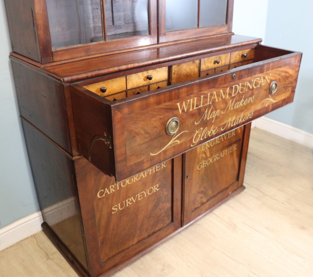A late Georgian mahogany secretaire bookcase with glazed upper doors featuring Roman numerals, a drop-front fitted writing desk, and two cabinet doors below. View XXII