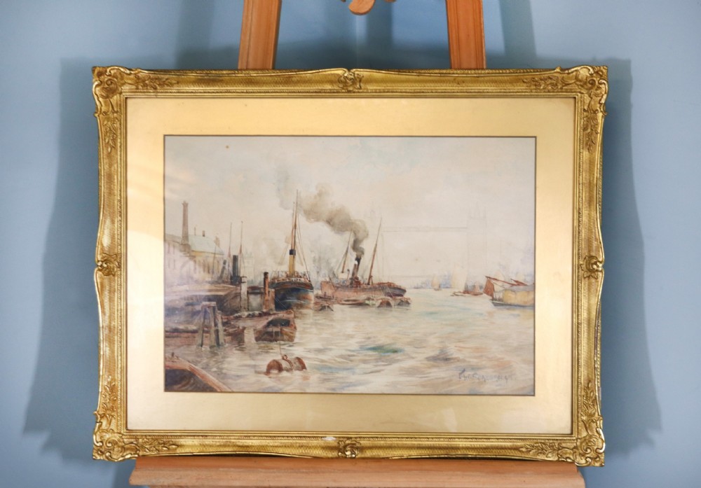 A framed maritime watercolour painting depicting steamships and barges on a river with Tower Bridge in the background, housed in a ornate gilded swept frame.
