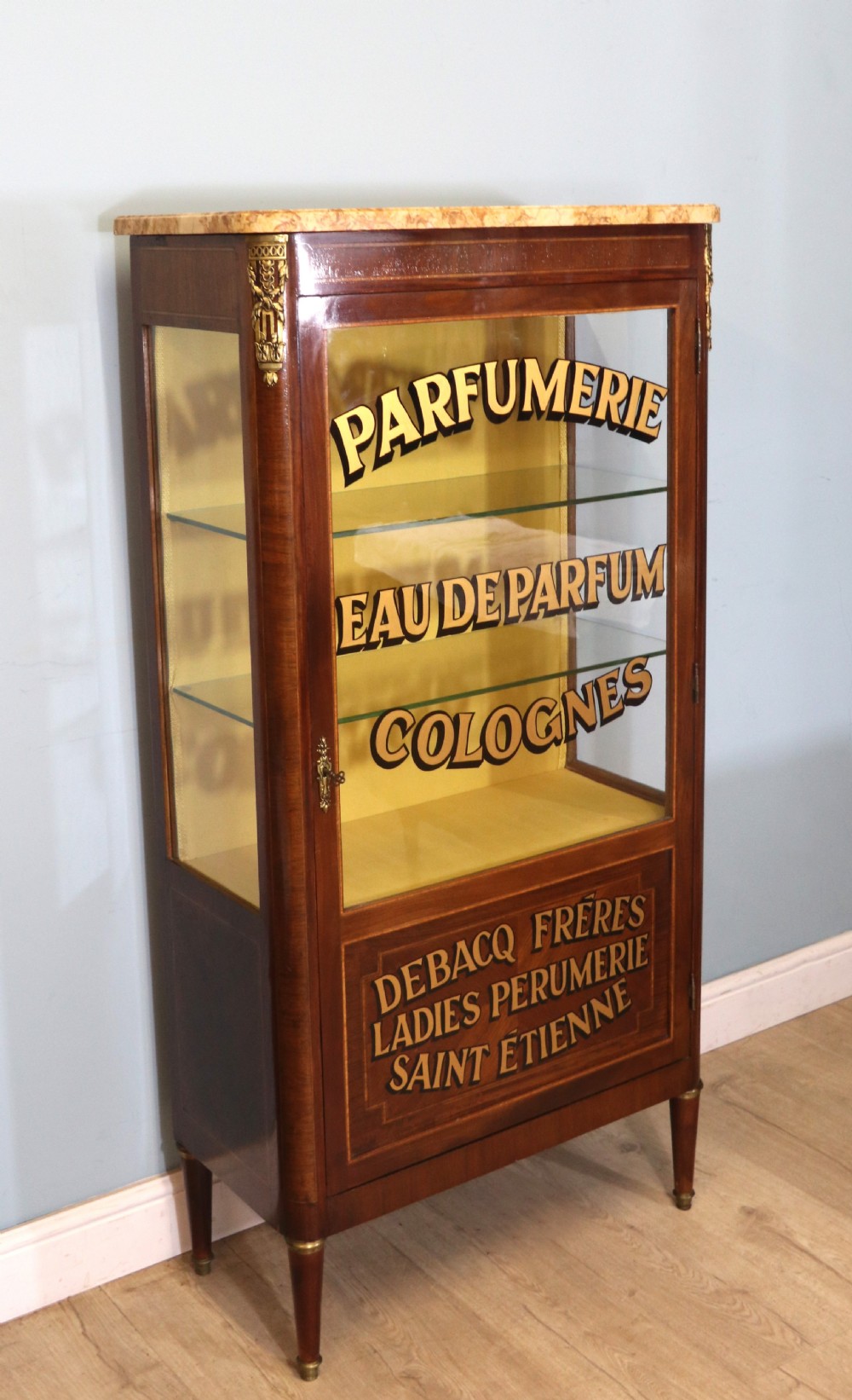 A French mahogany vitrine featuring a marble top, glass display door with gilt perfumery lettering, glass shelves, and brass mounts. View III