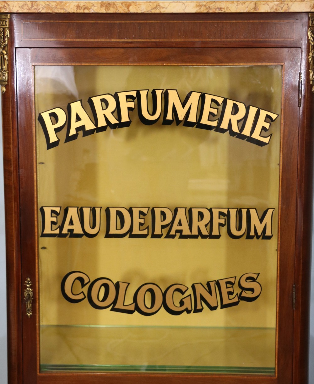 A French mahogany vitrine featuring a marble top, glass display door with gilt perfumery lettering, glass shelves, and brass mounts. View IX