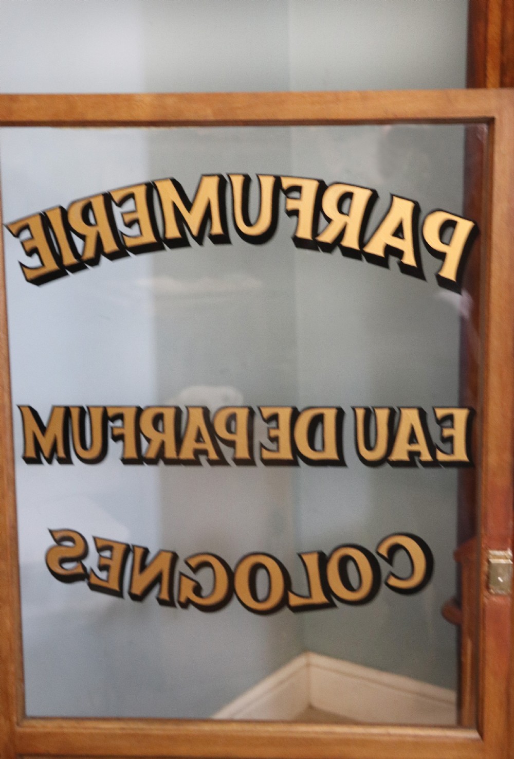 A French mahogany vitrine featuring a marble top, glass display door with gilt perfumery lettering, glass shelves, and brass mounts. View XV