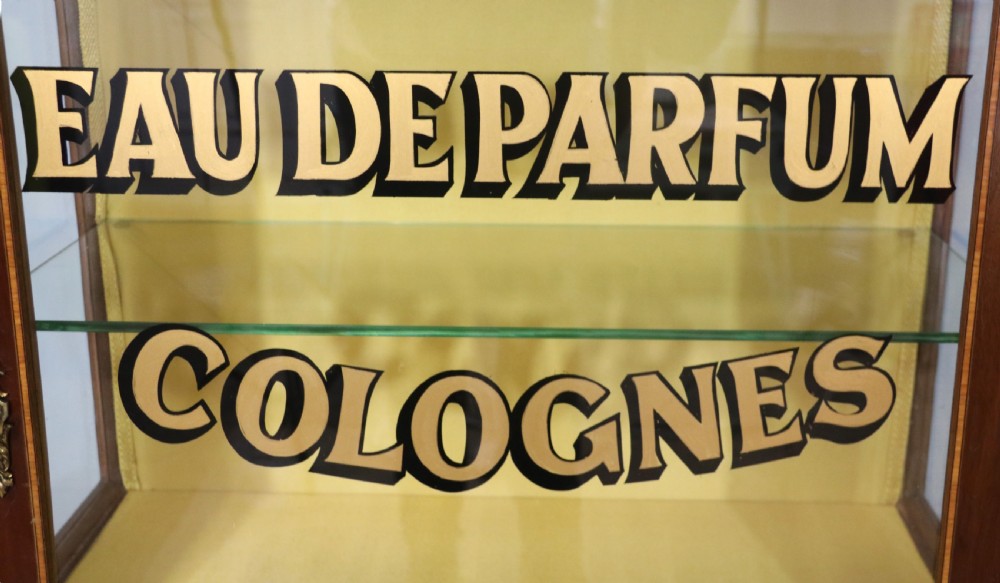 A French mahogany vitrine featuring a marble top, glass display door with gilt perfumery lettering, glass shelves, and brass mounts. View XVII