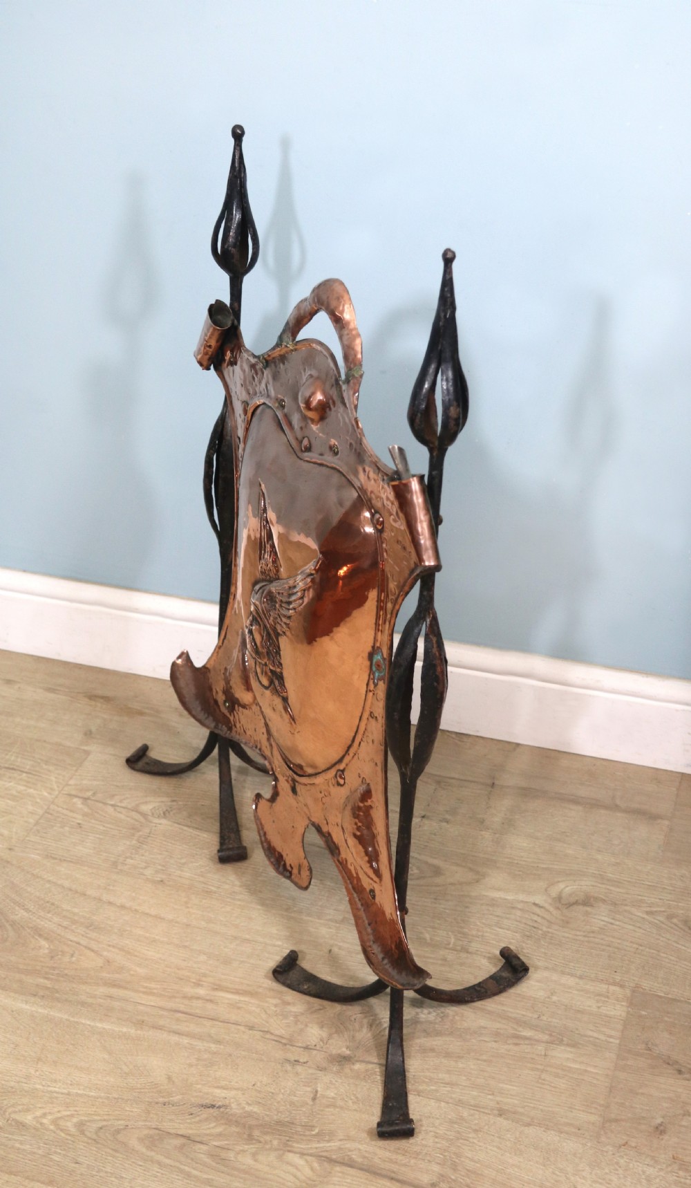 A 19th-century repousse copper panel fire screen featuring a winged warrior profile motif mounted in a wrought-iron frame with splayed feet. View II