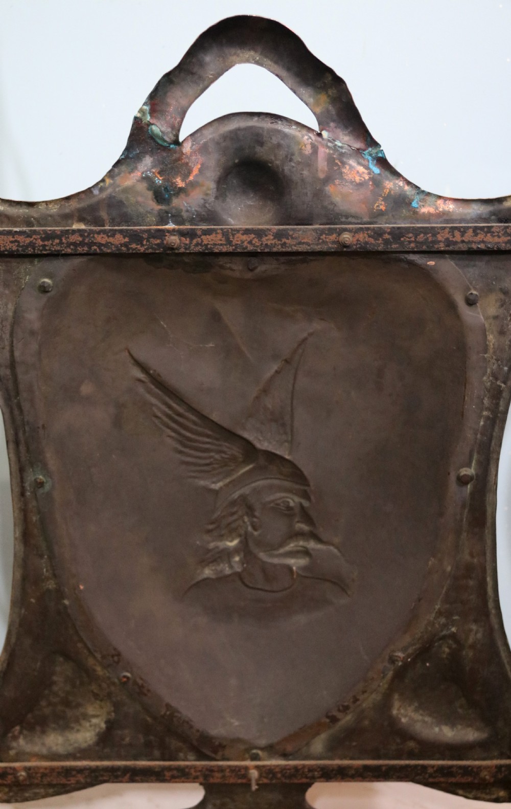 A 19th-century repousse copper panel fire screen featuring a winged warrior profile motif mounted in a wrought-iron frame with splayed feet. View III