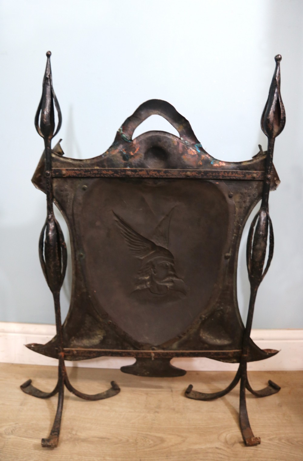 A 19th-century repousse copper panel fire screen featuring a winged warrior profile motif mounted in a wrought-iron frame with splayed feet. View IV