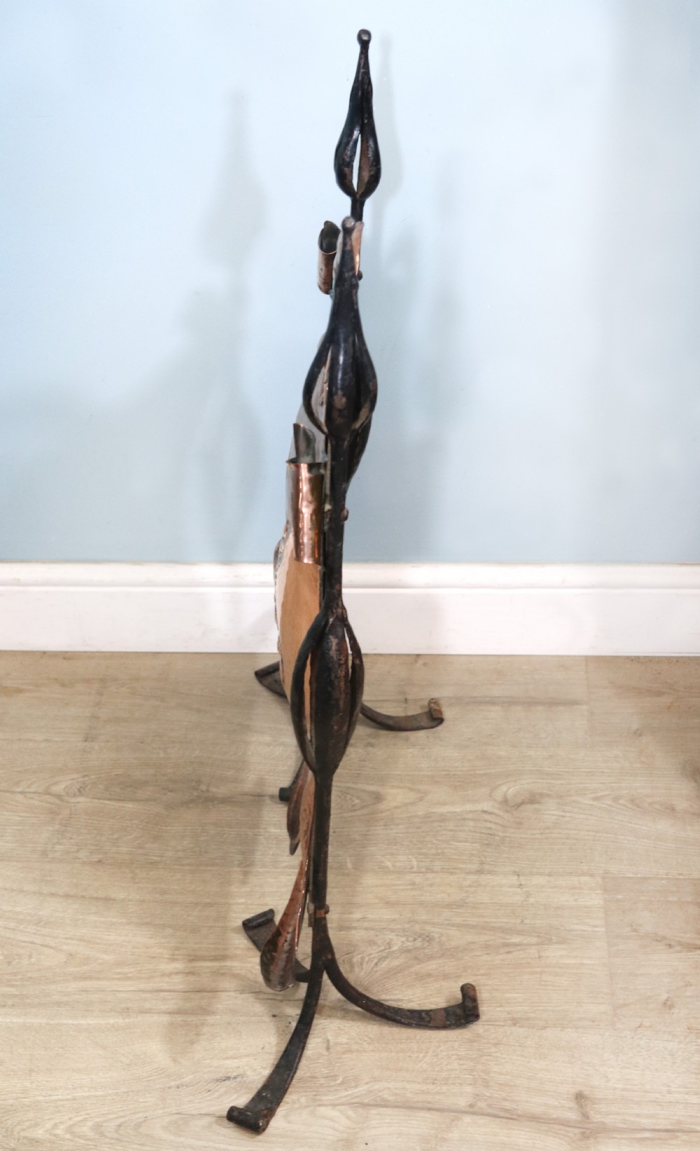 A 19th-century repousse copper panel fire screen featuring a winged warrior profile motif mounted in a wrought-iron frame with splayed feet. View V