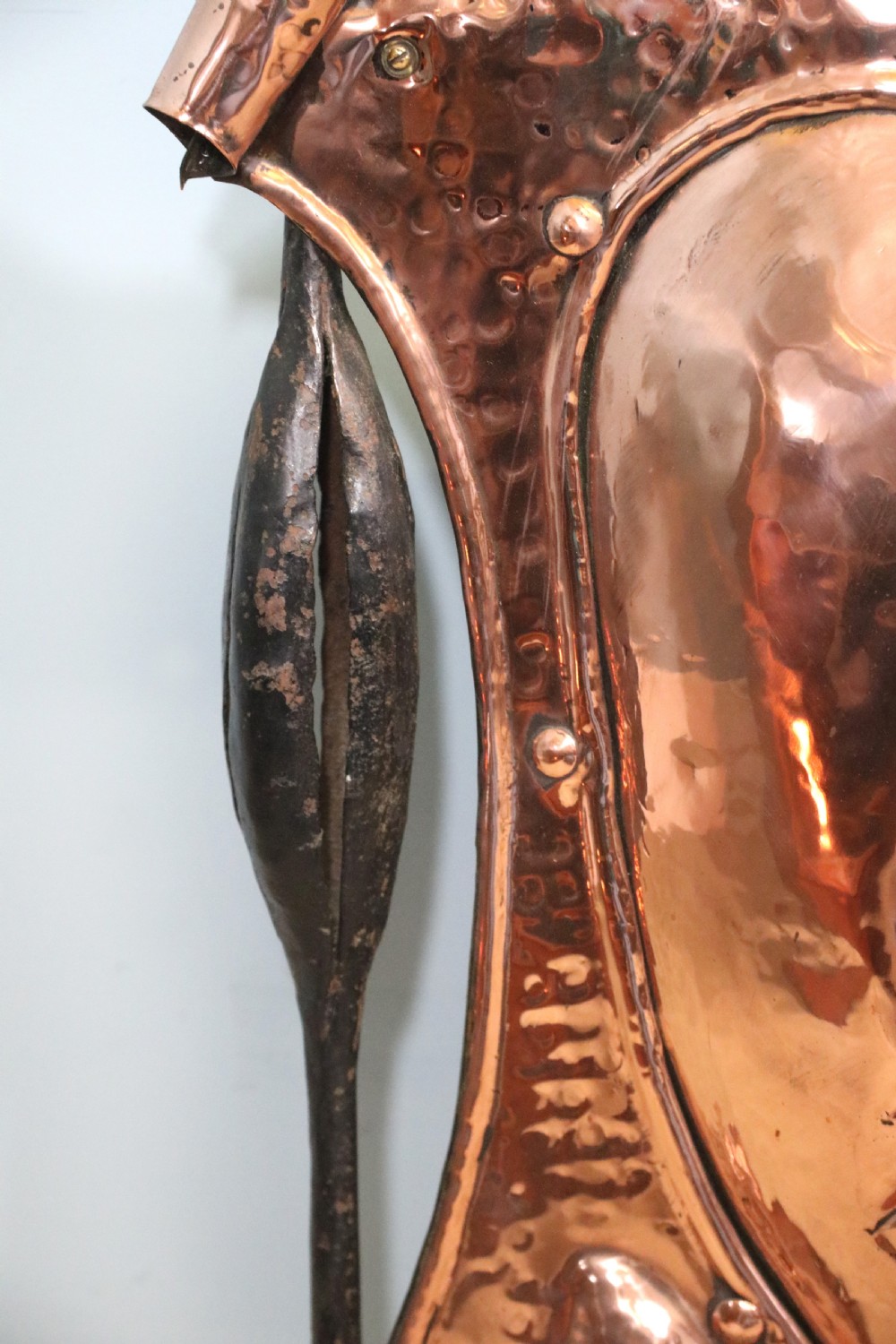 A 19th-century repousse copper panel fire screen featuring a winged warrior profile motif mounted in a wrought-iron frame with splayed feet. View X