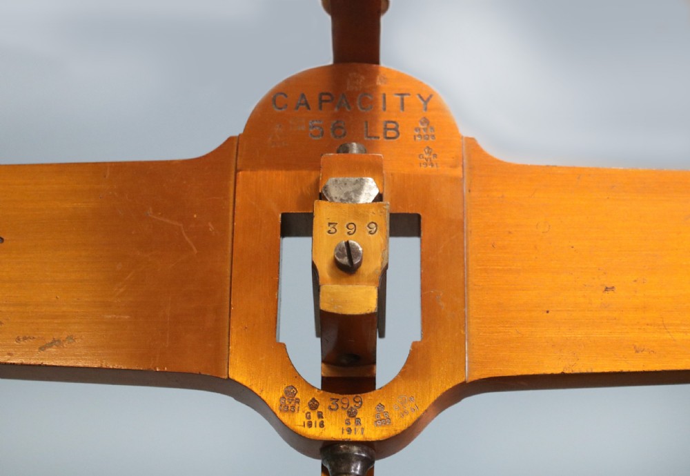 A large hanging brass beam balance scale featuring stamped lettering, suspended chain links, and two circular brass pans. View IX