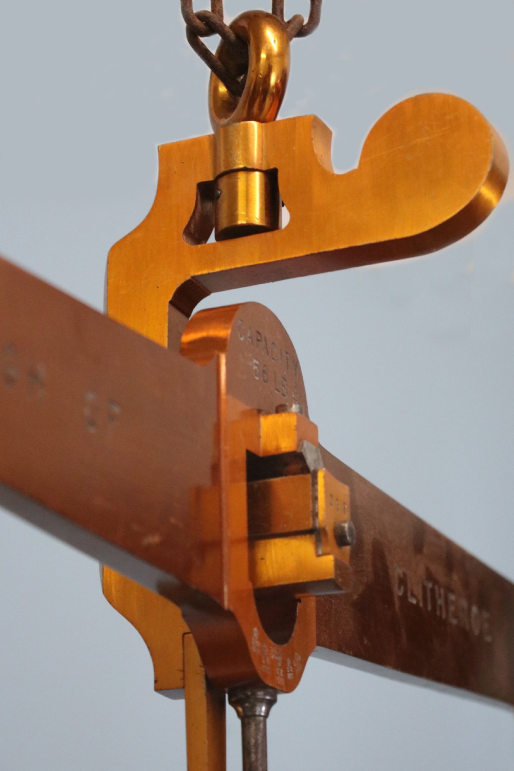 A large hanging brass beam balance scale featuring stamped lettering, suspended chain links, and two circular brass pans. View XV