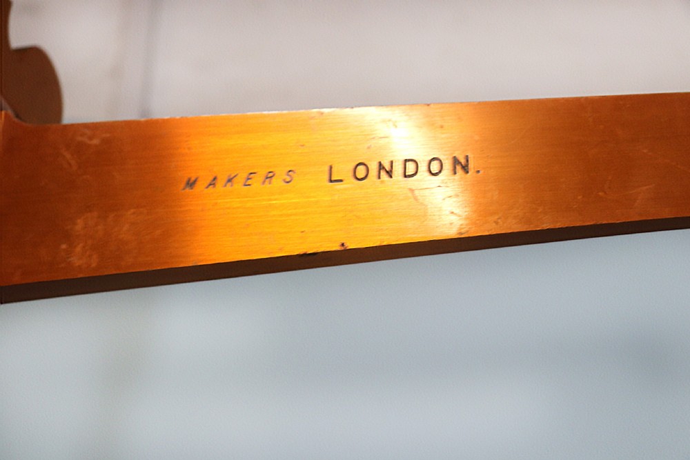 A large hanging brass beam balance scale featuring stamped lettering, suspended chain links, and two circular brass pans. View XVI