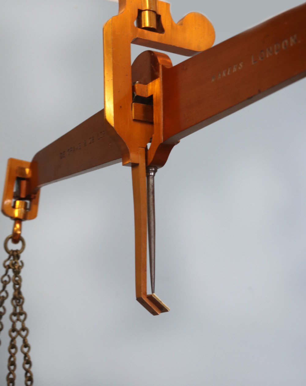 A large hanging brass beam balance scale featuring stamped lettering, suspended chain links, and two circular brass pans. View XIX