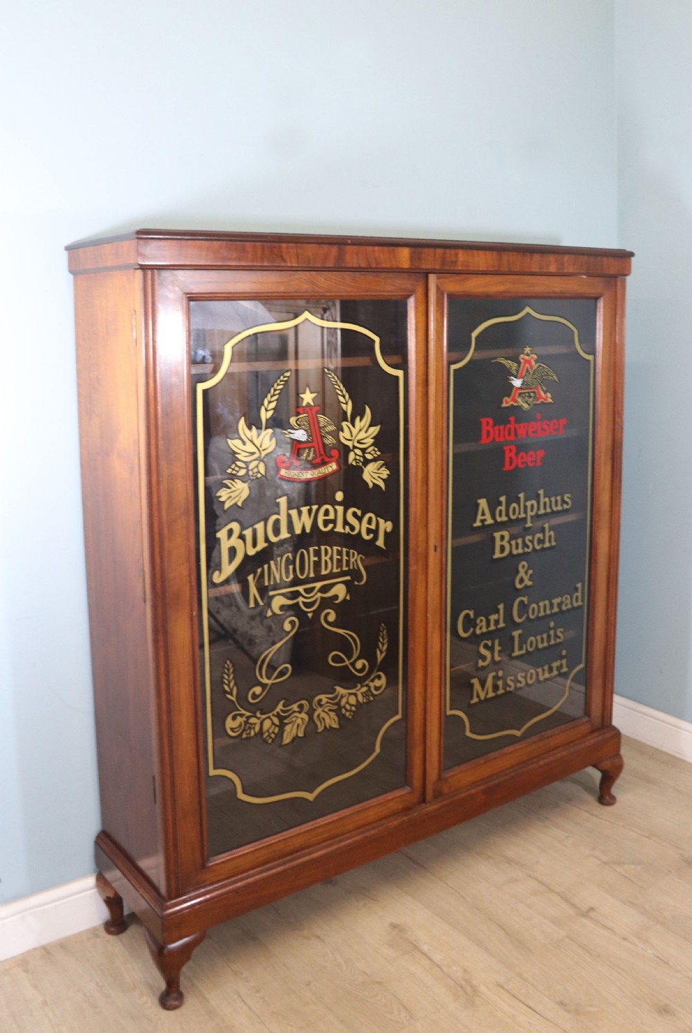 An early 20th-century walnut glazed display cabinet featuring two glass doors with gilded Budweiser advertising signwriting and cabriole legs. View II