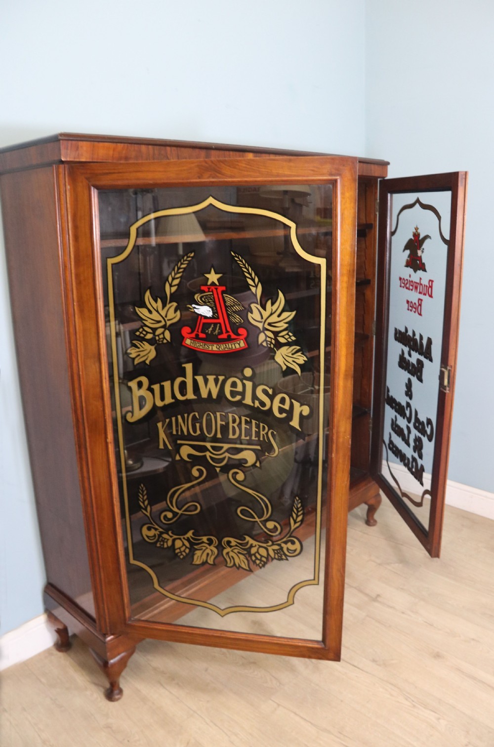 An early 20th-century walnut glazed display cabinet featuring two glass doors with gilded Budweiser advertising signwriting and cabriole legs. View III