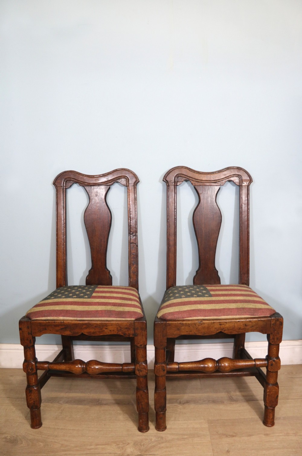 A pair of dark oak side chairs featuring vasiform back splats, turned front stretchers, and seats upholstered in an American flag pattern fabric.