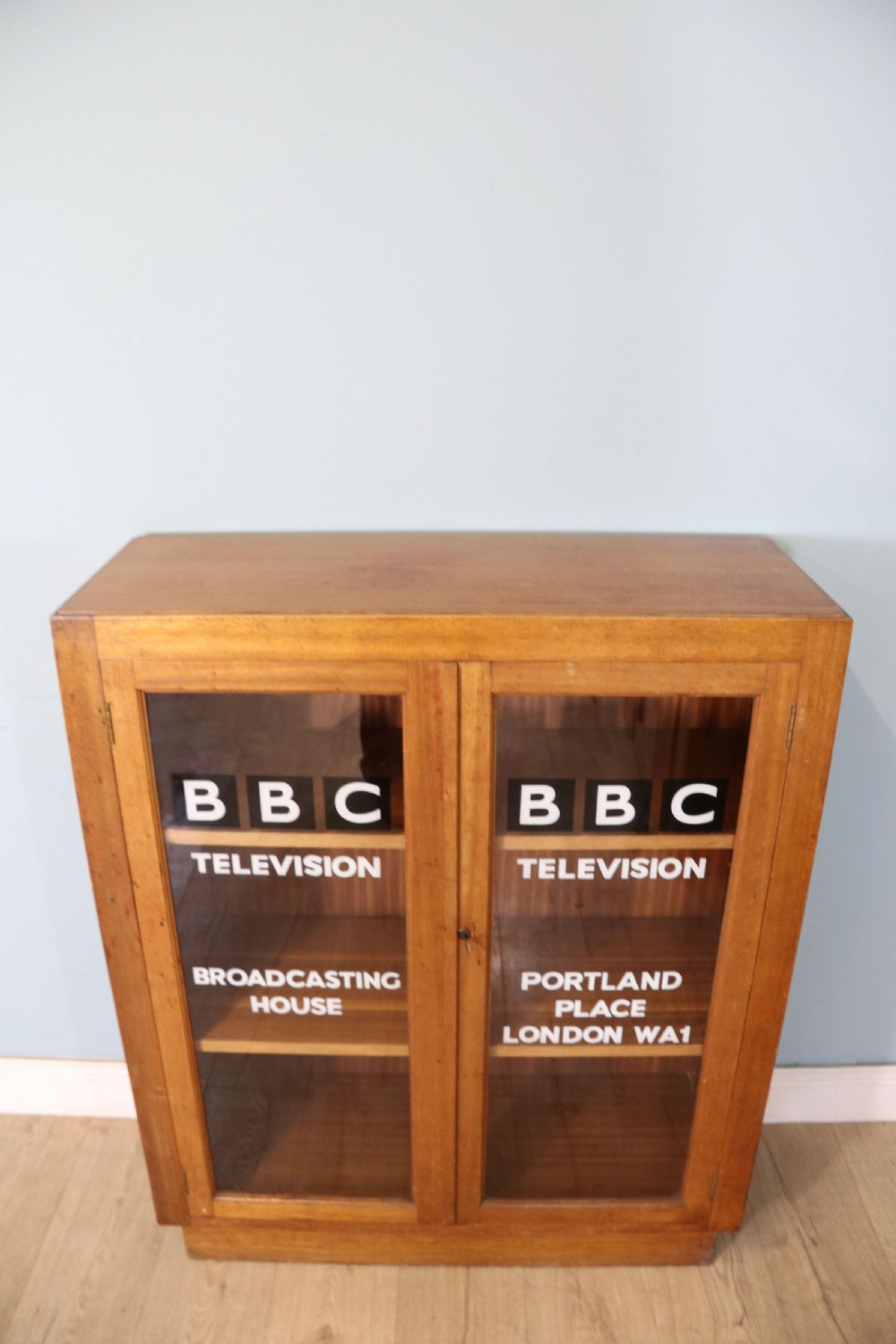 A 1930s light mahogany two-door glazed bookcase featuring white lettering on glass panels set over an enclosed wooden base. View II