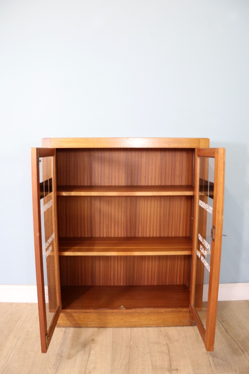 A 1930s light mahogany two-door glazed bookcase featuring white lettering on glass panels set over an enclosed wooden base. View III