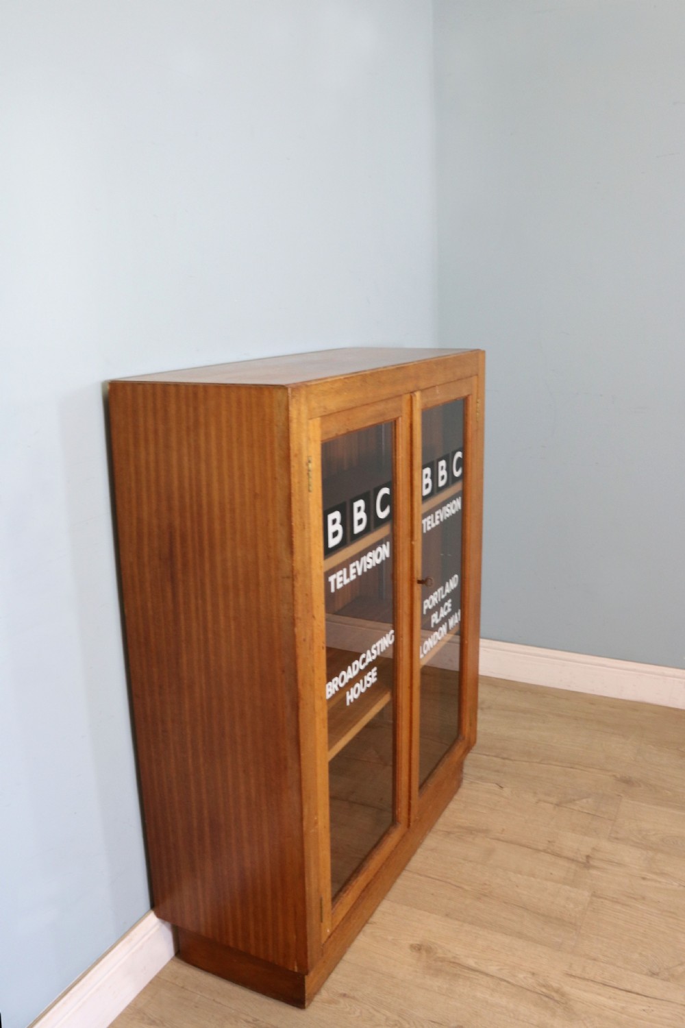 A 1930s light mahogany two-door glazed bookcase featuring white lettering on glass panels set over an enclosed wooden base. View IV