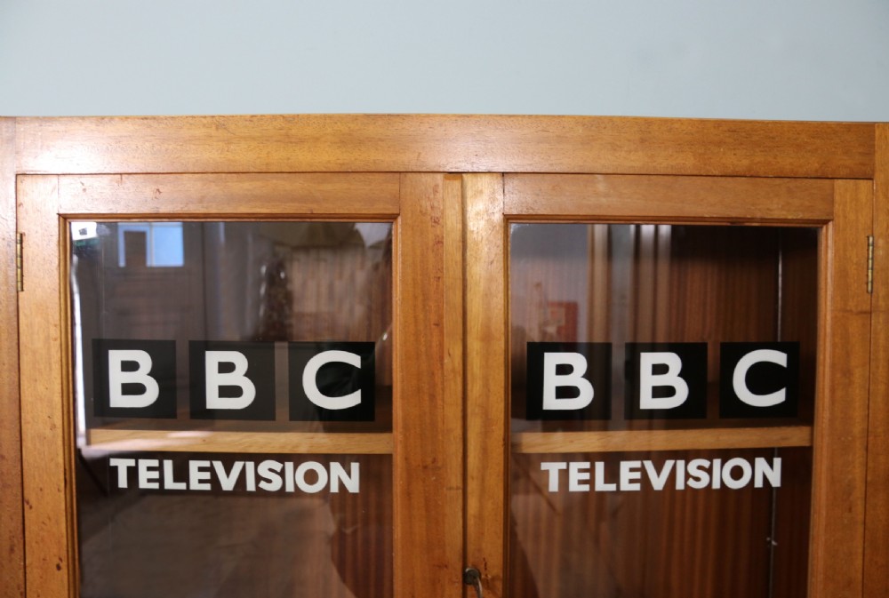 A 1930s light mahogany two-door glazed bookcase featuring white lettering on glass panels set over an enclosed wooden base. View VI