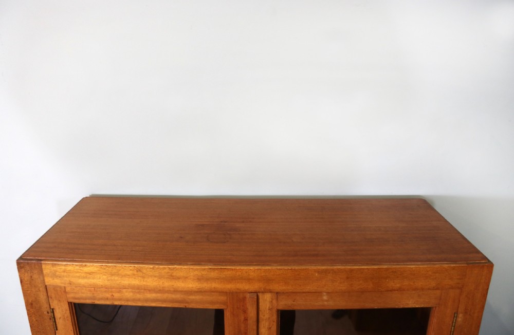 A 1930s light mahogany two-door glazed bookcase featuring white lettering on glass panels set over an enclosed wooden base. View X