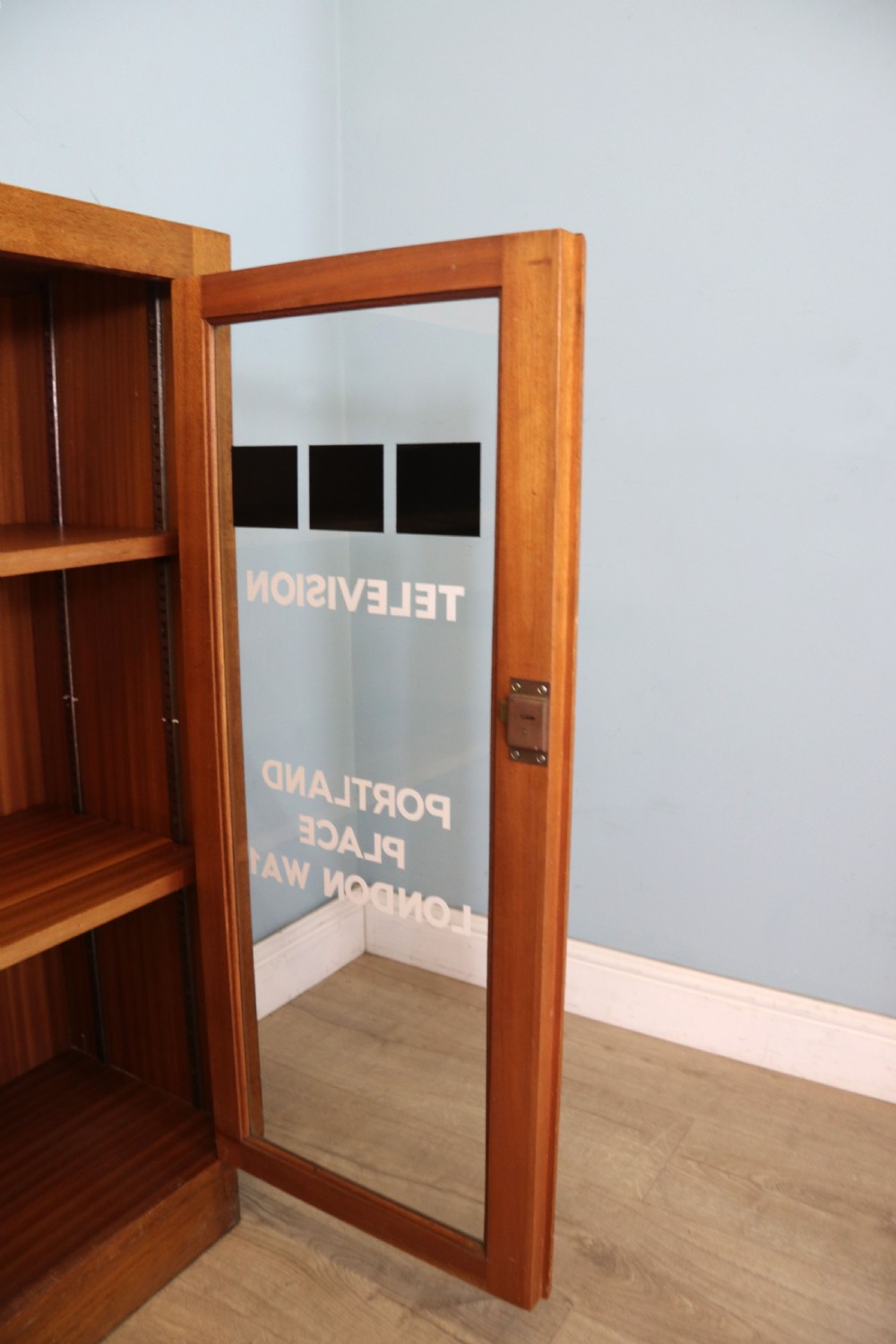 A 1930s light mahogany two-door glazed bookcase featuring white lettering on glass panels set over an enclosed wooden base. View XIV