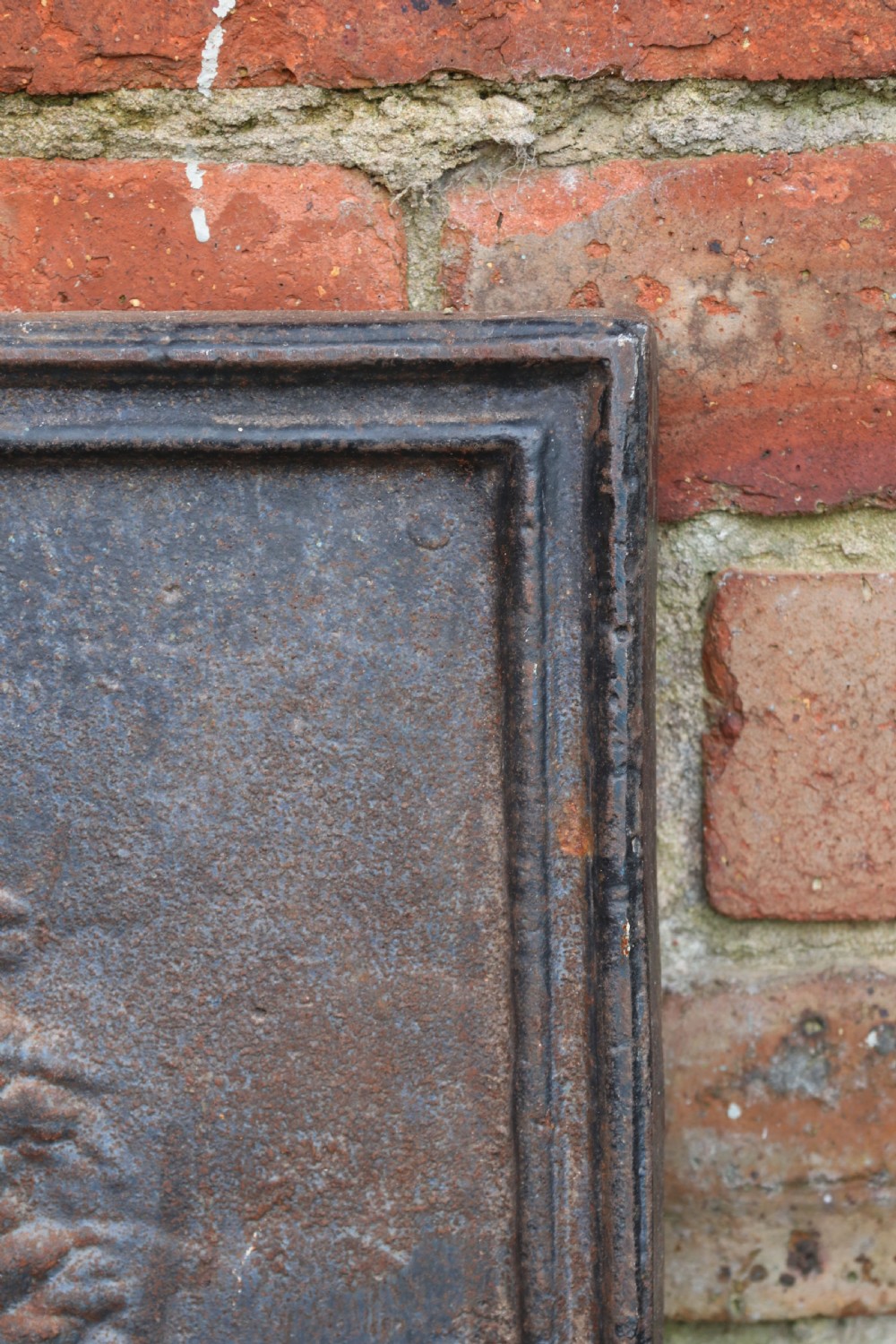 A square cast iron fireback featuring a raised relief scene of cherubs and putti beneath a leafy tree surrounded by a moulded border. View VIII