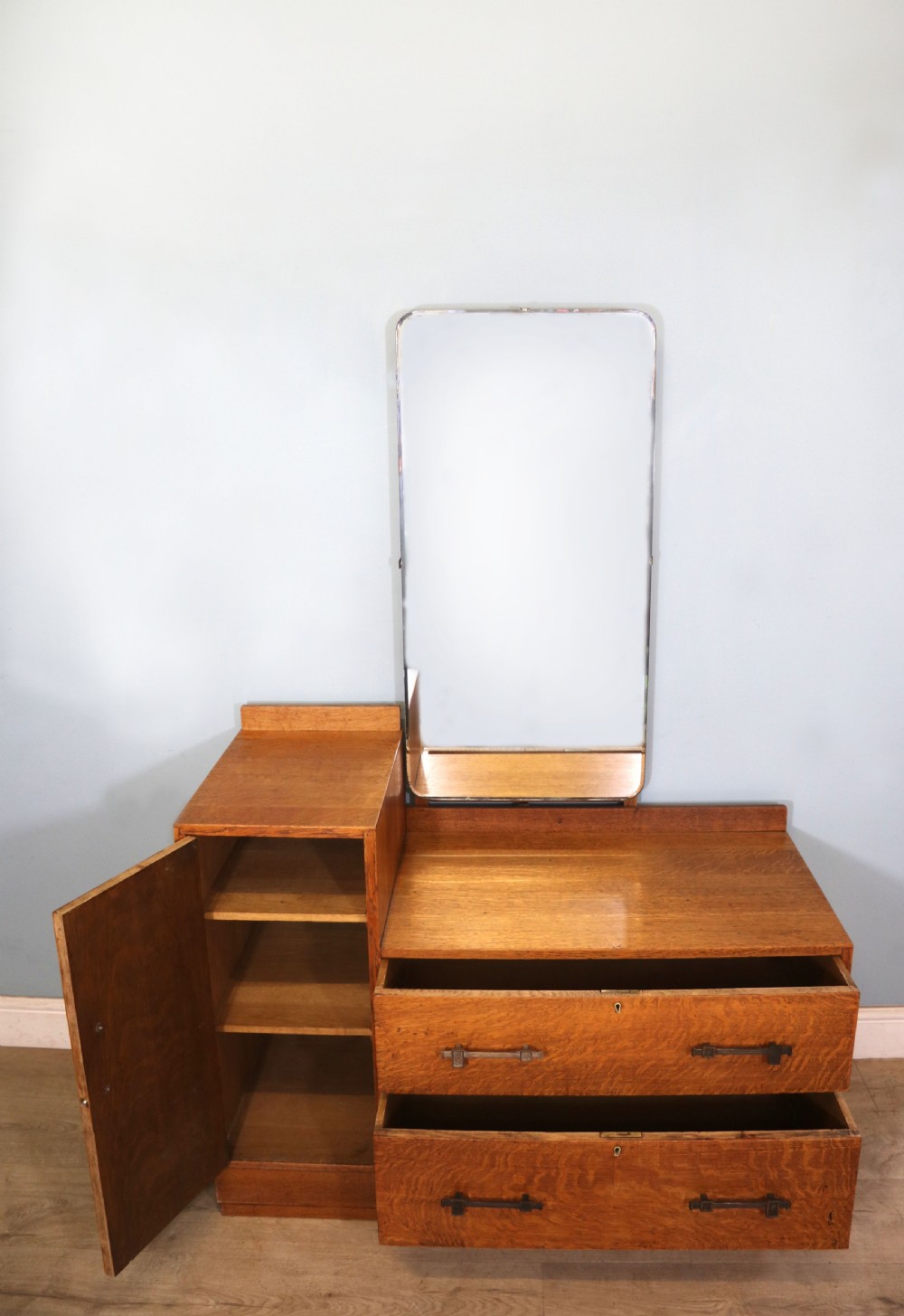 An asymmetrical golden oak dressing chest with a left-hand side cupboard, two drawers on the right, metal handles, and an off-centre tall mirror. View II