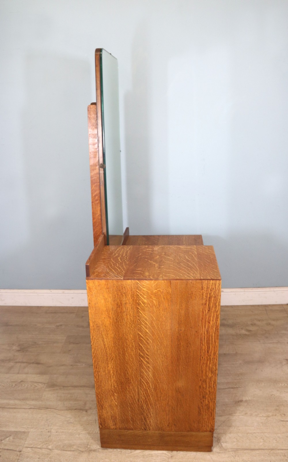 An asymmetrical golden oak dressing chest with a left-hand side cupboard, two drawers on the right, metal handles, and an off-centre tall mirror. View VI