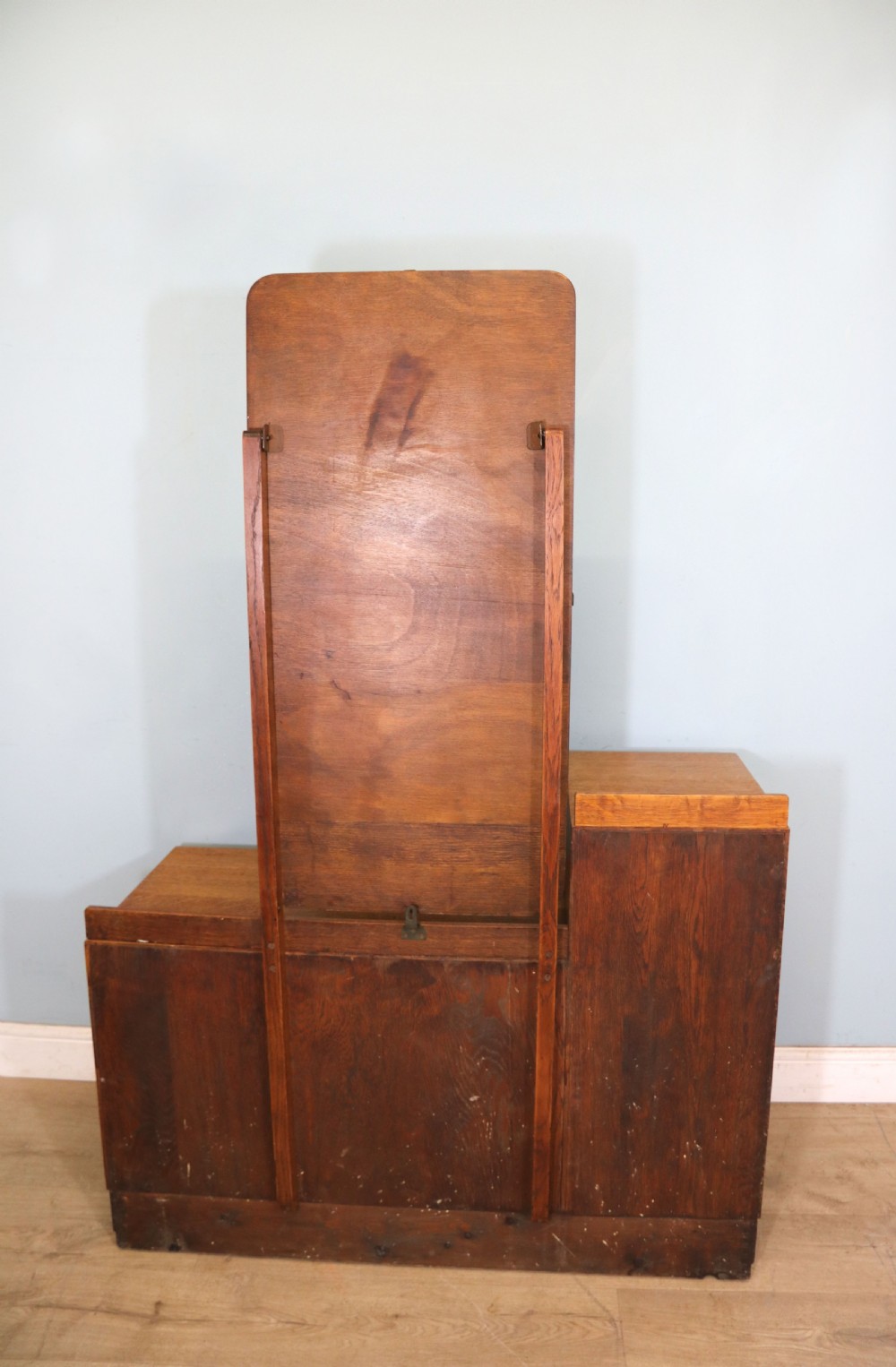 An asymmetrical golden oak dressing chest with a left-hand side cupboard, two drawers on the right, metal handles, and an off-centre tall mirror. View VII