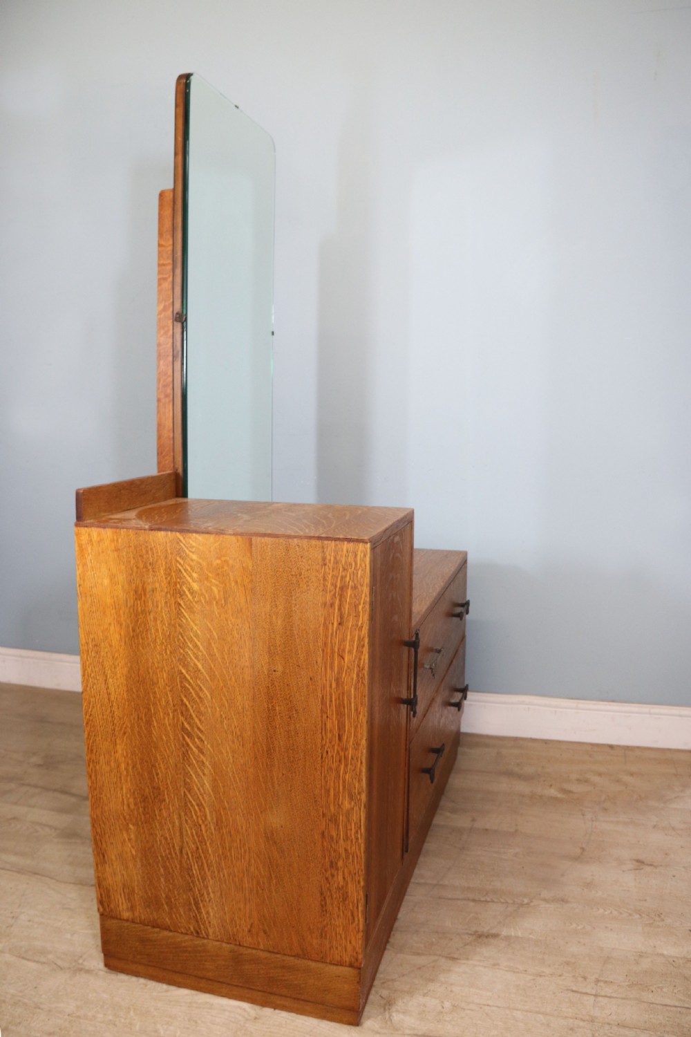 An asymmetrical golden oak dressing chest with a left-hand side cupboard, two drawers on the right, metal handles, and an off-centre tall mirror. View VIII
