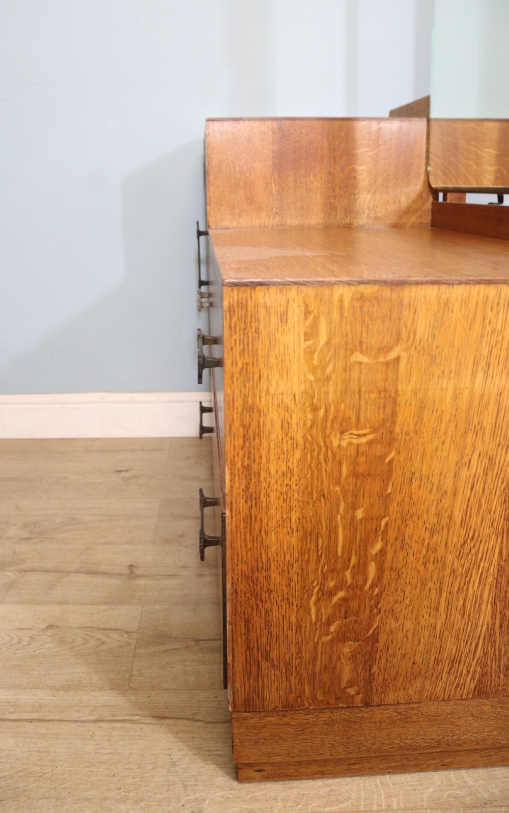 An asymmetrical golden oak dressing chest with a left-hand side cupboard, two drawers on the right, metal handles, and an off-centre tall mirror. View XVI