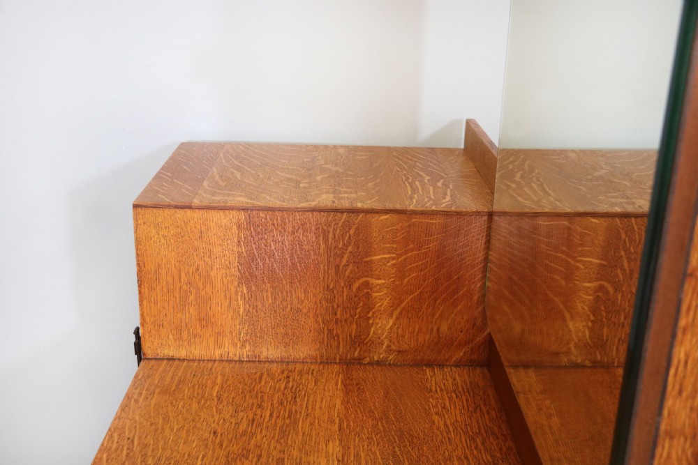 An asymmetrical golden oak dressing chest with a left-hand side cupboard, two drawers on the right, metal handles, and an off-centre tall mirror. View XVII