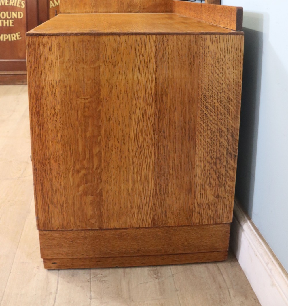 An asymmetrical golden oak dressing chest with a left-hand side cupboard, two drawers on the right, metal handles, and an off-centre tall mirror. View XXIV