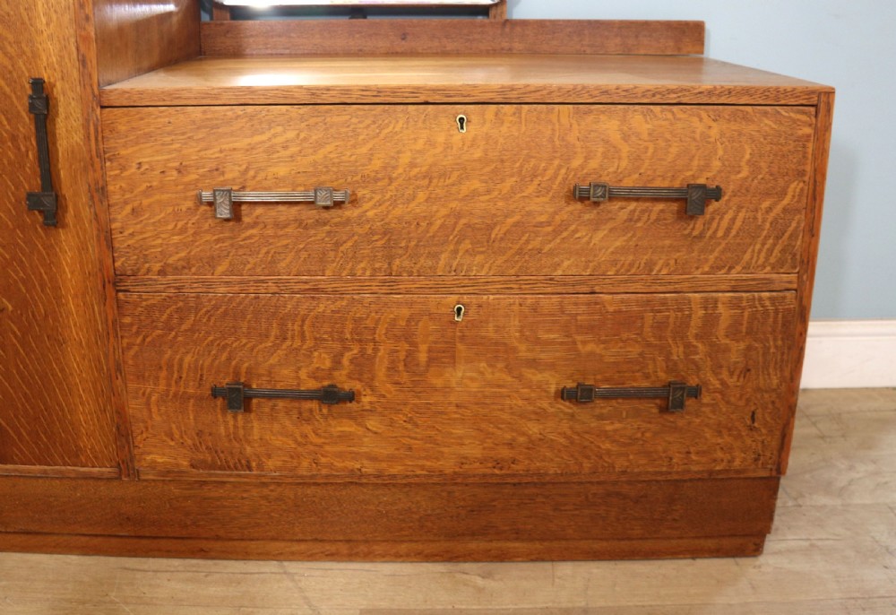 An asymmetrical golden oak dressing chest with a left-hand side cupboard, two drawers on the right, metal handles, and an off-centre tall mirror. View XXIX